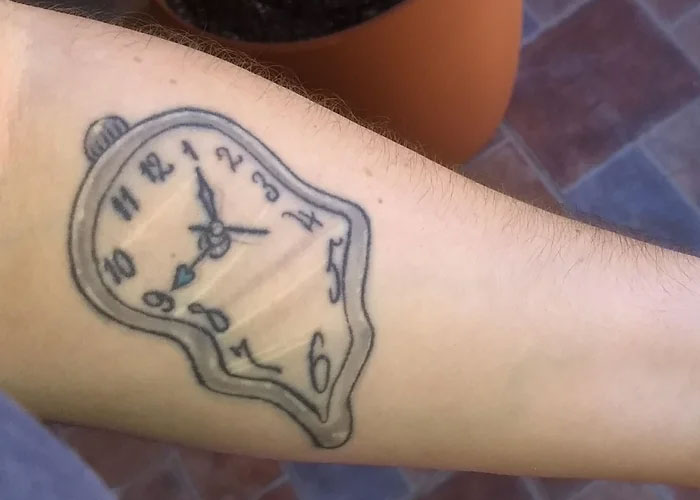 A melting clock tattoo design on an arm, often seen as lacking creativity.