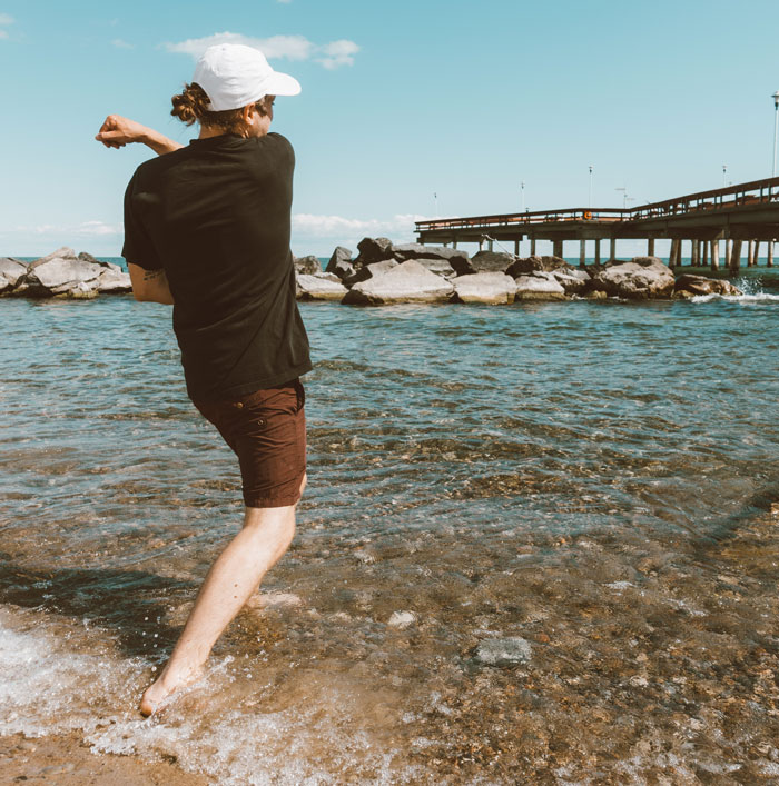 Man skipping stones in ocean, a weird hobby enjoyed in spare time, with a pier in the background.
