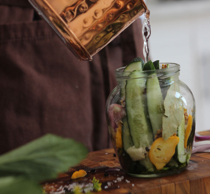 Person engaging in the weird hobby of pickling, pouring water into a jar of cucumbers.