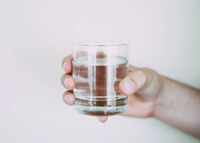 Hand holding a clear glass of water illustrating unusual guest rules or weirdest rules at someone's house.