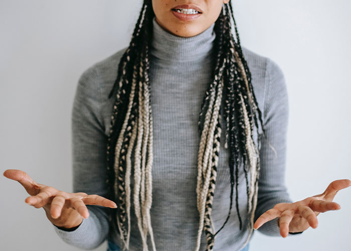 Person with long braided hair in a gray turtleneck gesturing with open hands about weird guest house rules.