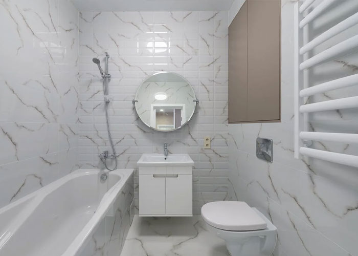 Modern bathroom with white marble tiles, bathtub, round mirror, and toilet illustrating guest house rules and weird experiences.