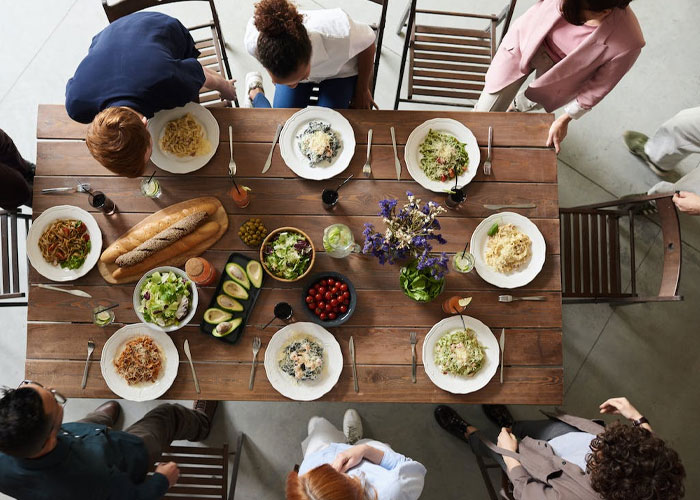 Group of people sitting around a wooden table with food, illustrating weird guest rules at someone’s house.