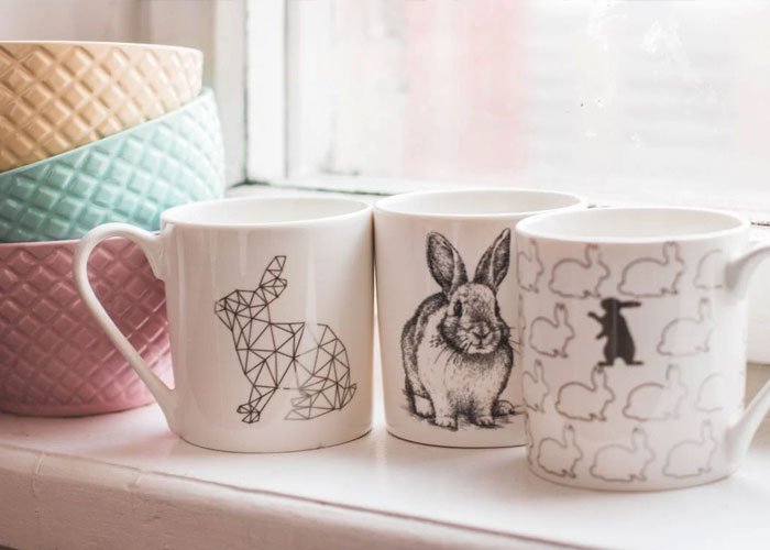 Three ceramic mugs with different rabbit designs sit on a windowsill, illustrating weird guest house rules.