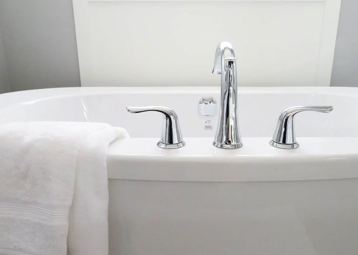 Modern bathtub faucet with a white towel draped over the edge symbolizing weird house guest rules.