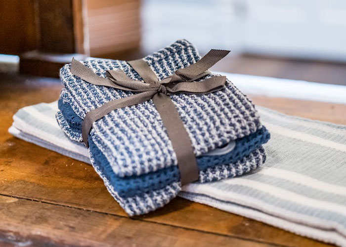 Stack of folded kitchen towels tied with a ribbon on a wooden table, illustrating weird guest house rules.