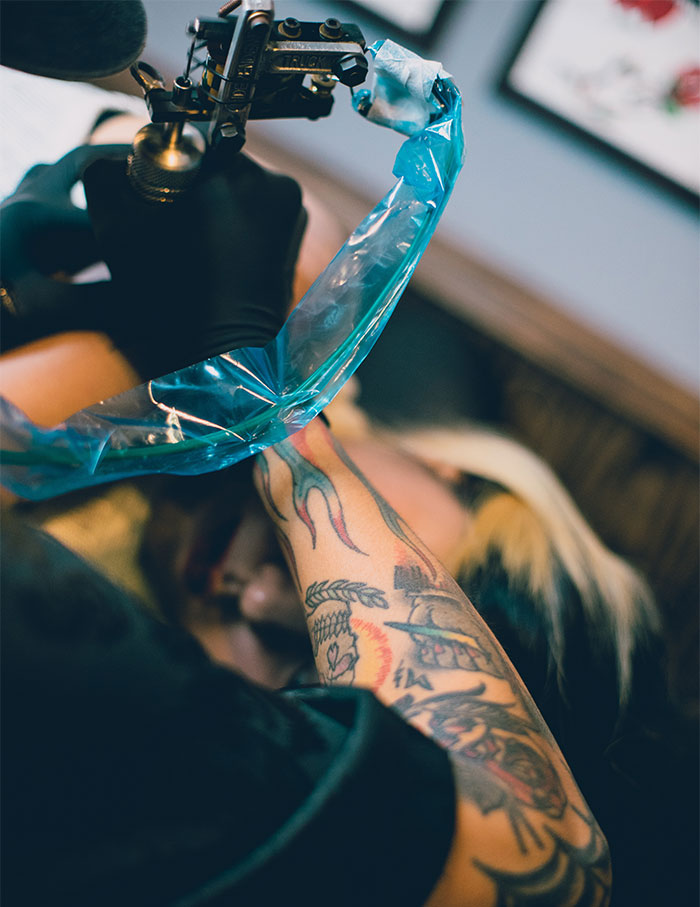 Tattoo artist inking a colorful design on a woman's arm in a studio setting.