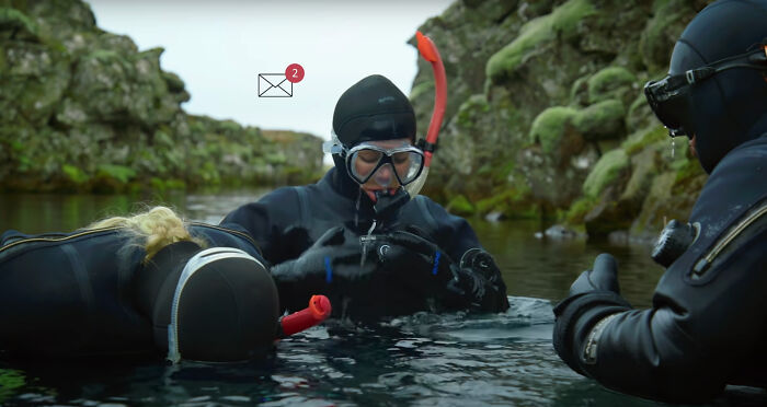 Divers in wetsuits receiving email notification in an Icelandic mossy landscape setting.