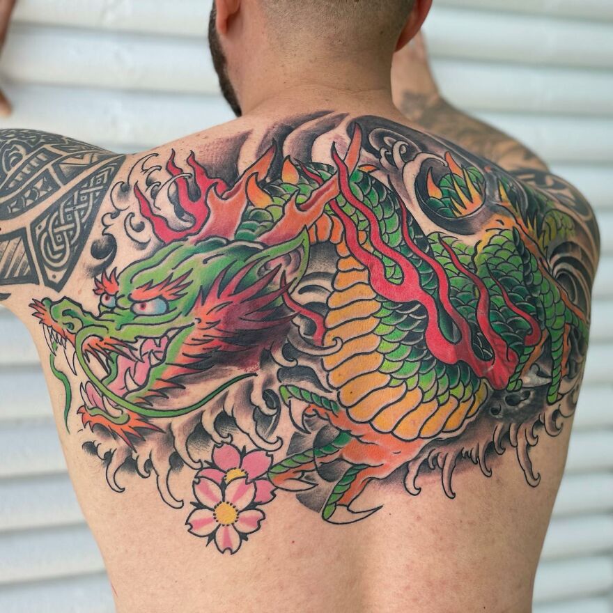 Colorful dragon tattoo covering a man's back, with intricate scales and flames.