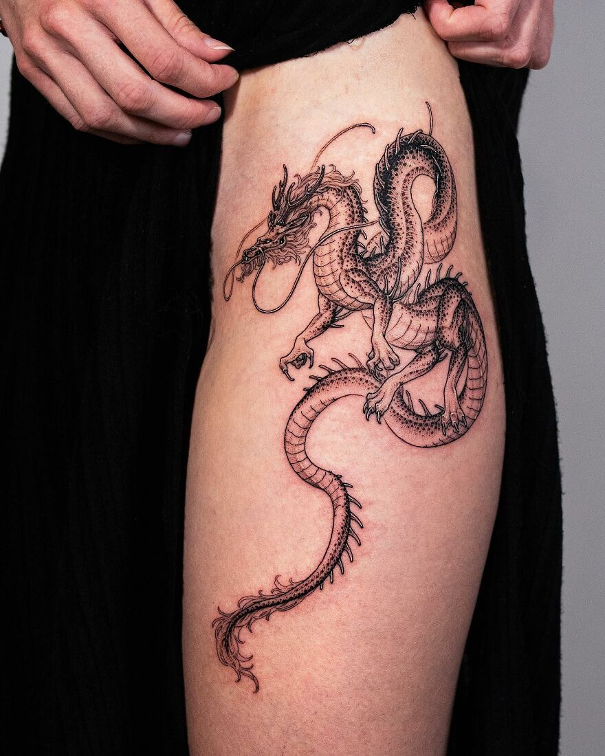 Detailed dragon tattoo design on a person's upper thigh, showcasing intricate line work and shading.