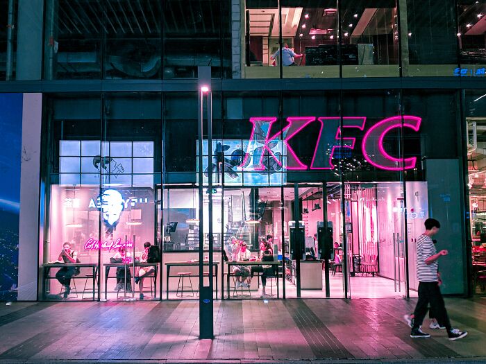 Exterior view of KFC restaurant at night with neon lights, people dining inside, illustrating weird and interesting facts.