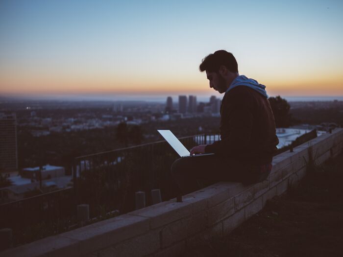 Silhouette of a person using a laptop outdoors at sunset, reflecting on the worst trend that has ever existed.