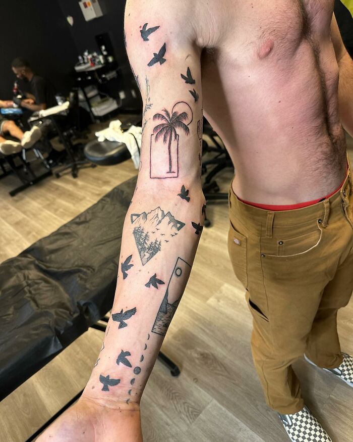 Person with arm showcasing unique patchwork tattoo design, featuring birds, palm tree, and mountains in a modern style.
