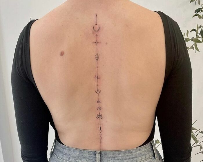 Elegant design of a minimalist spine tattoo on a person's back, featuring geometric and celestial elements.