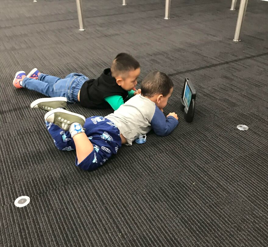 Two kids layin on the ground and watching something on a tablet 