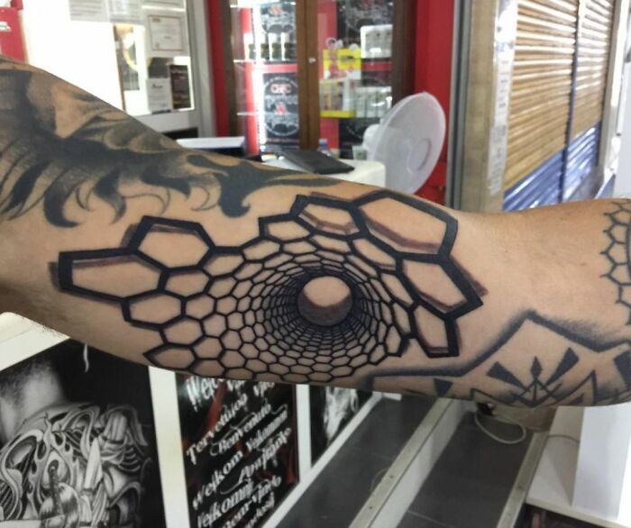 Arm with an epic optical illusion tattoo design featuring a hexagonal tunnel pattern in a tattoo studio setting.