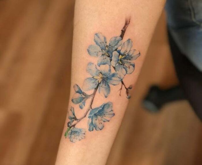Blue flower tattoo blossoming on forearm skin.