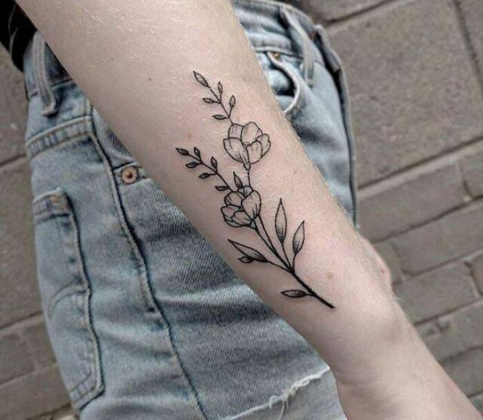 Minimalist flower tattoo on a person's arm with denim shorts background.
