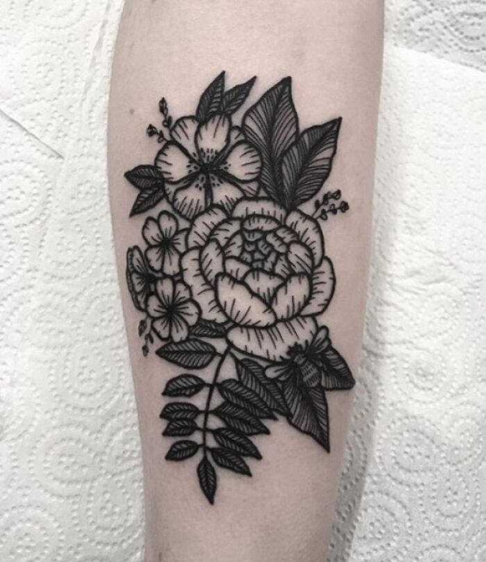 Black ink flower tattoo design on forearm, featuring blooming blossoms and detailed leaves.