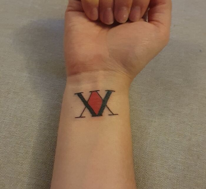 Wrist tattoo featuring a Roman numeral design in black and red ink.