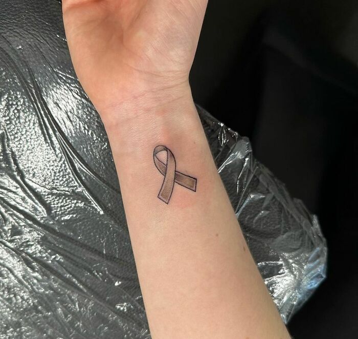 Wrist tattoo of a simple ribbon design on inner arm.
