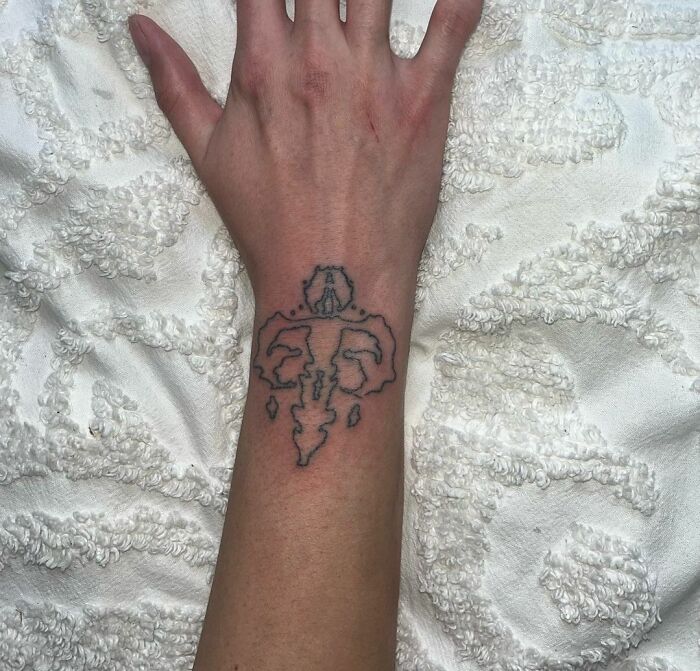 Abstract wrist tattoo design featuring a unique symbol on a textured white background.