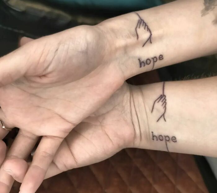Minimalist wrist tattoo with the word "hope" and intertwined hands.