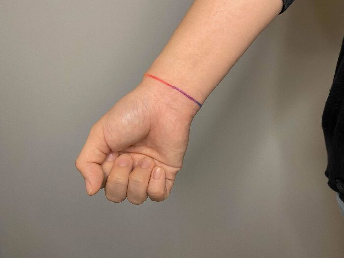 Minimalist wrist tattoo with red and purple lines.