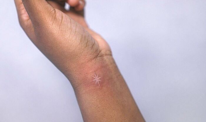 A delicate wrist tattoo design featuring a small, white ink star.
