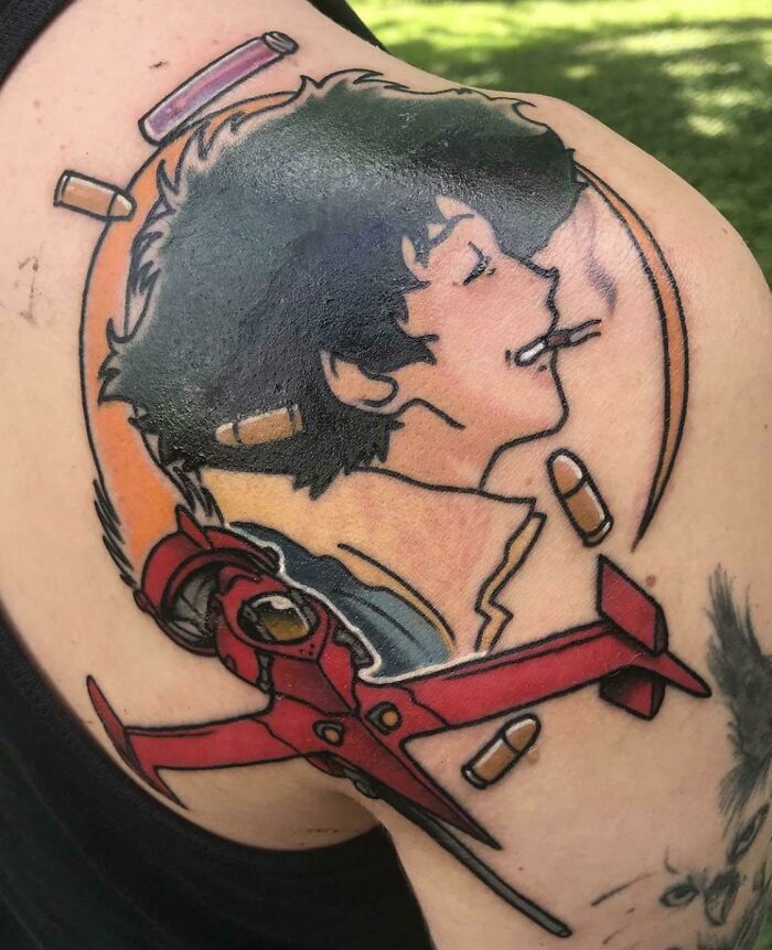 Pop culture tattoo of an animated character with a red spaceship and bullets, inked on an upper arm.