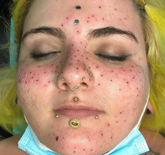 Face with multiple piercings and tattoos, closed eyes, showcasing permanent inked mistakes.