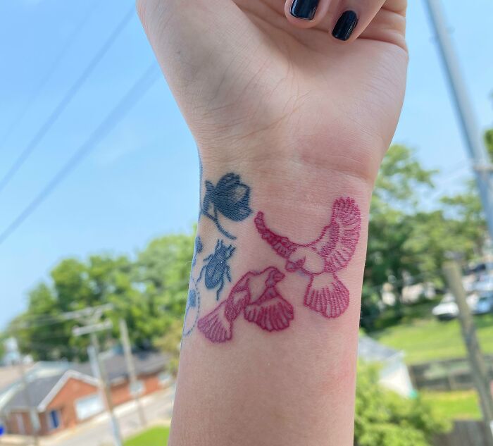 Colorful bird wrist tattoo design with a blue flower in the background.