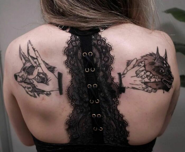 Back tattoos depicting hand holding a wolf head, showcasing pop culture art style.