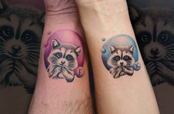 Matching raccoon tattoos on wrists, symbolizing a special bond.