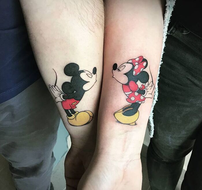 Matching tattoos of Mickey and Minnie Mouse on a couple's arms, symbolizing their special bond.