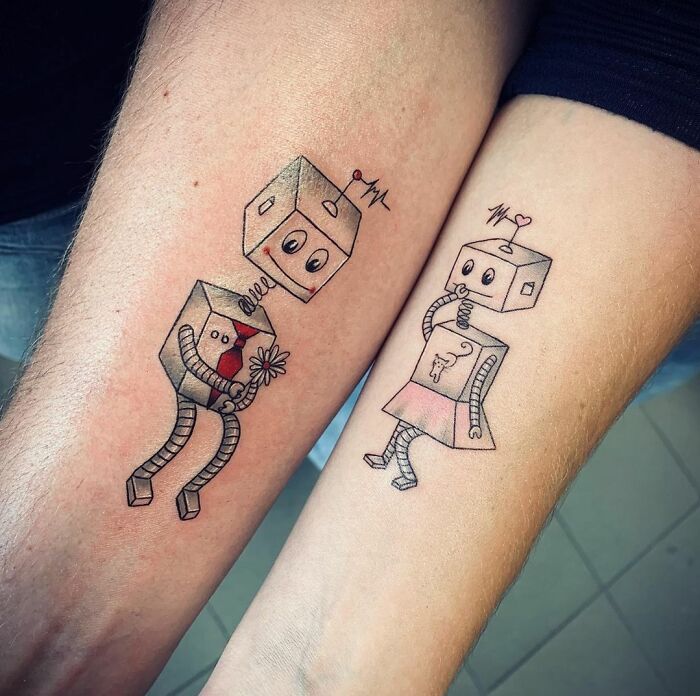 Matching tattoos of cute robot characters on two arms, symbolizing a special bond.