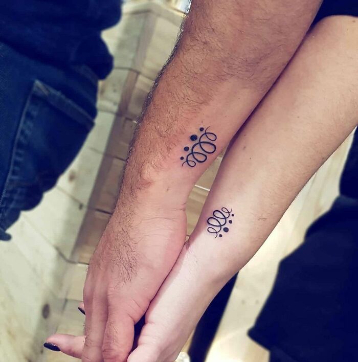 Matching tattoos on two arms with an abstract design, symbolizing connection and unity.