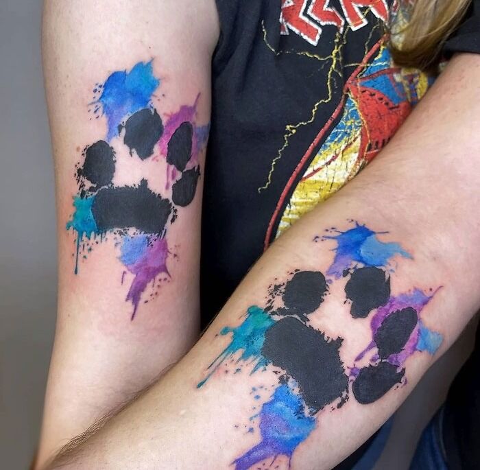 Colorful matching tattoos for couples featuring watercolor paw prints on forearms.