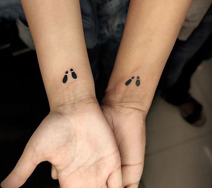 Matching tattoos on wrists featuring small black footprints for special people in your life.