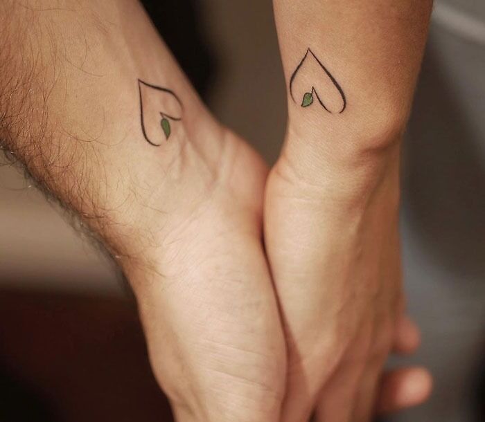 Matching tattoos of two minimalist heart designs with a small green leaf, symbolizing connection and love.