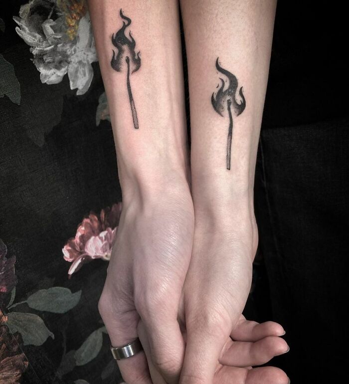 Matching tattoos of flames on two forearms, symbolizing a bond between people.