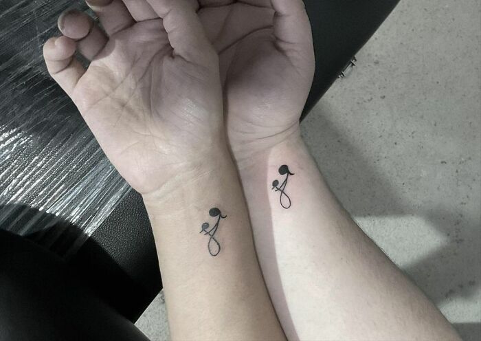 Matching tattoos on wrists, featuring small black flowers, symbolizing connection and special bond.