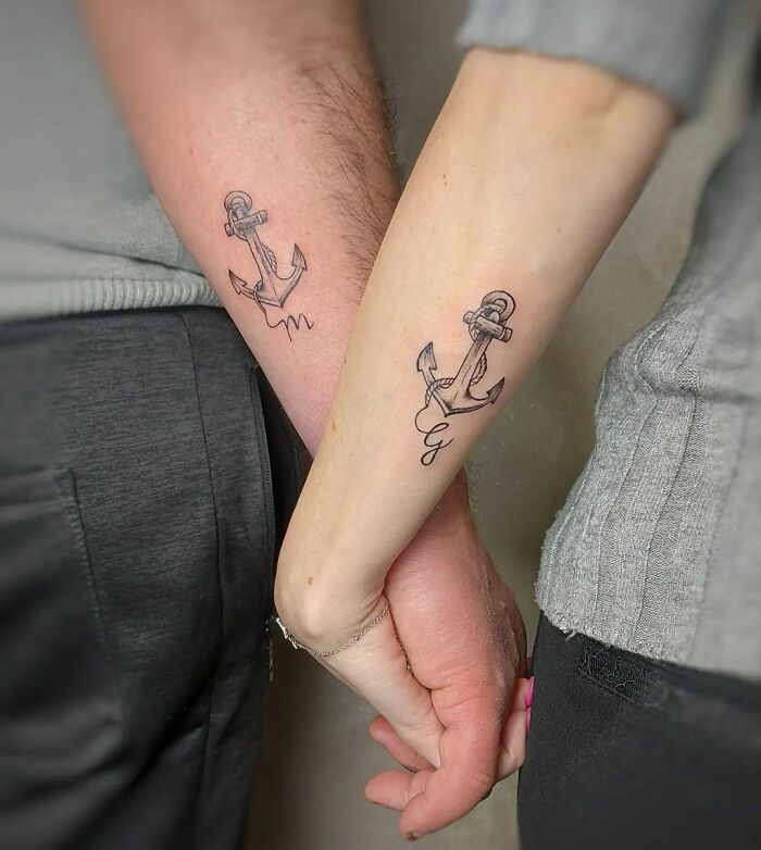 Matching anchor tattoos on couple's arms, symbolizing connection and commitment.