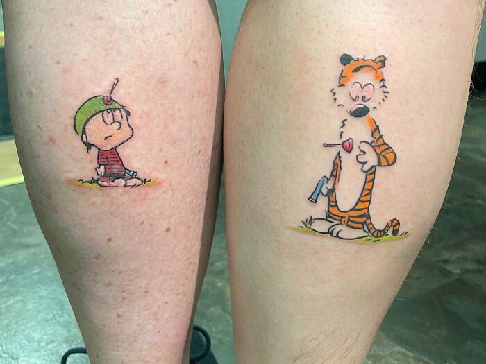 Matching tattoos of cartoon characters on two calves, symbolizing special bonds.