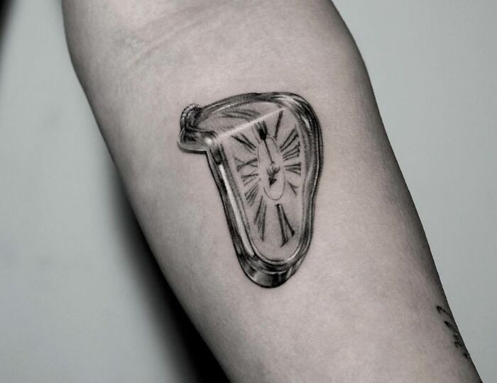 Melting clock tattoo on forearm, inspired by pop culture art.