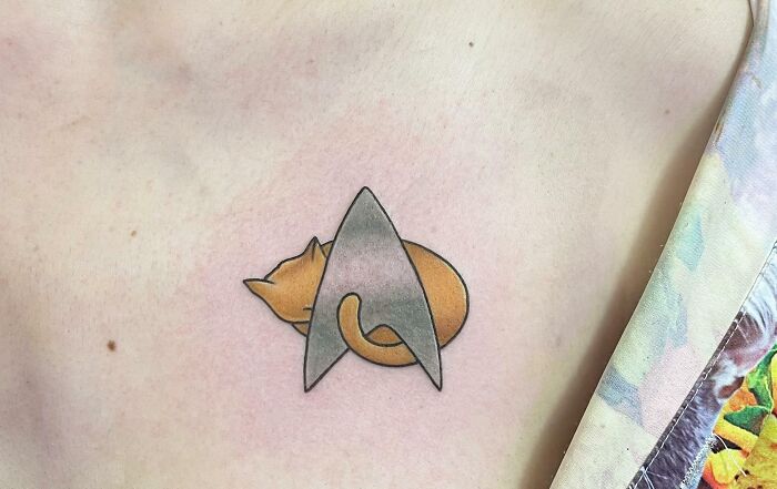Pop culture tattoo of a cat intertwined with a Star Trek emblem on someone's shoulder.