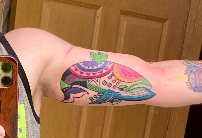Colorful pop culture tattoo of a geometric whale design on a person's inner bicep, photographed indoors.