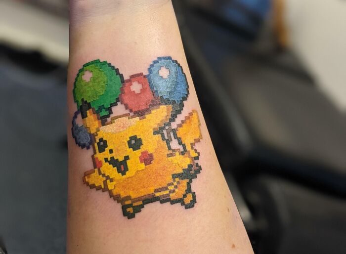 Pixelated pop culture tattoo of Pikachu with balloons on forearm.