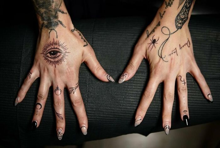 Small hand tattoos with intricate designs on both hands, featuring symbols and an eye motif.