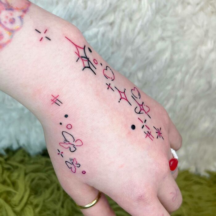 Hand with small tattoos, including stars, hearts, and butterflies, showcasing minimalist tattoo art.